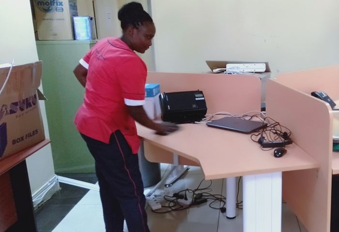 Cleaner dusting an office desk and equipment
