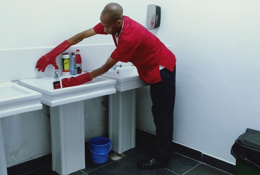 Cleaner wiping down washroom sink basins